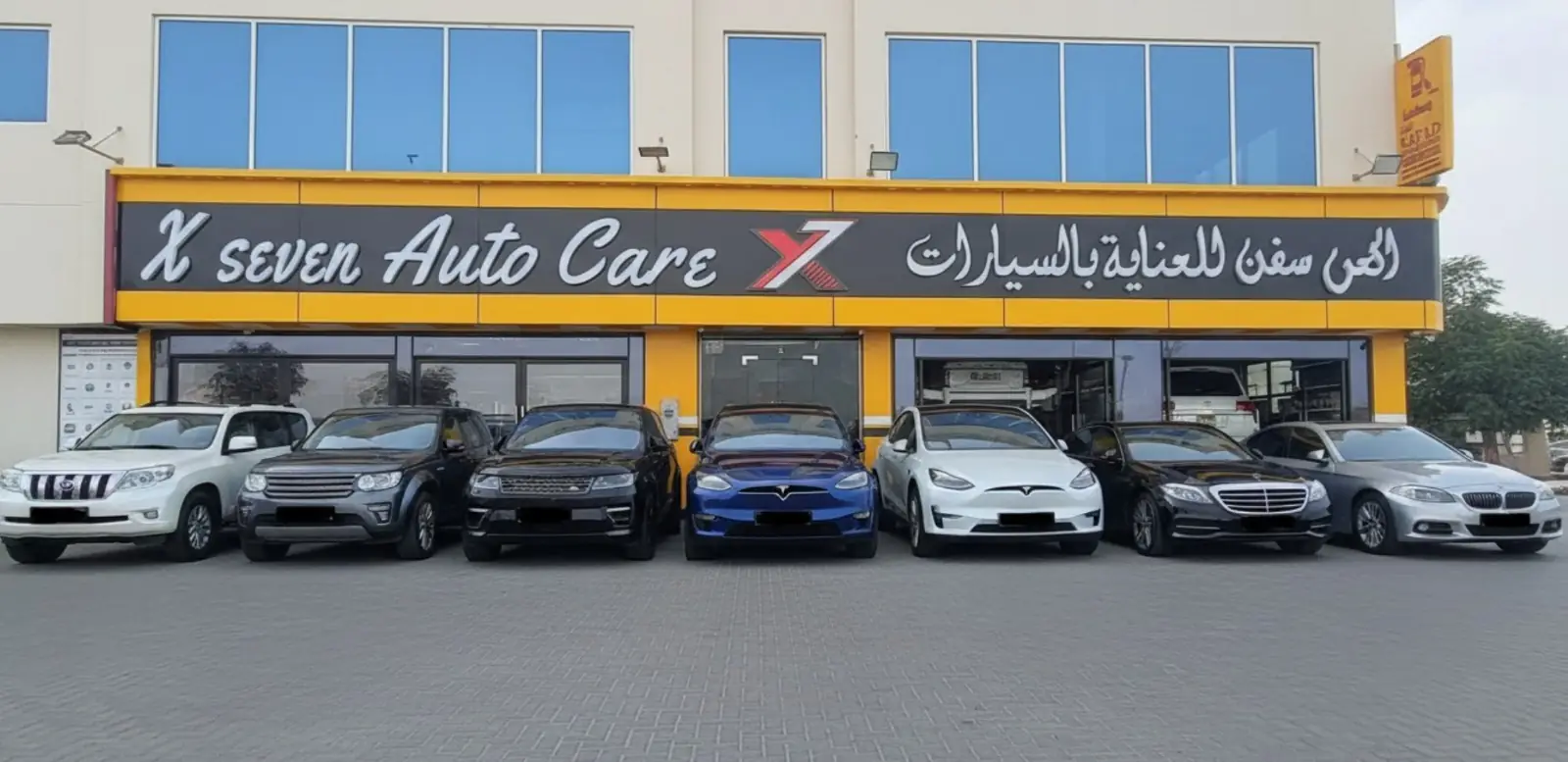 X7 Auto Care storefront in Khalifa City, Abu Dhabi with luxury cars including Tesla, BMW, Range Rover parked in front